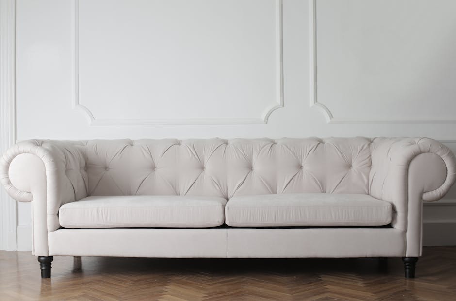 A close-up view of a beige fabric sofa located in a room with plain white walls, showing clean, well-maintained upholstery with a tufted design. The sofa's surface appears freshly cleaned, with no vis